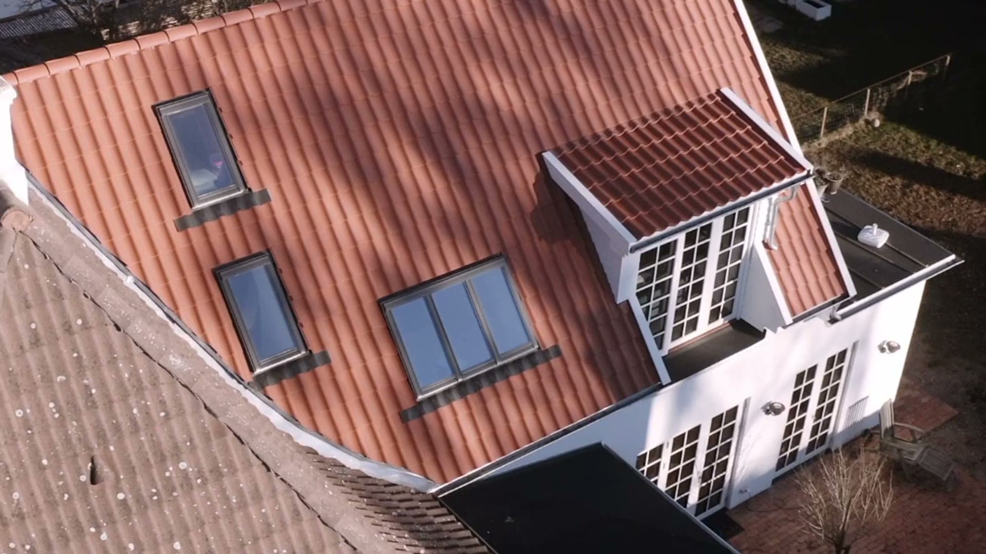 A tiled roof seen from above in winter sun, with three roof windows set into it and a white dormer with glazed doors at the end, gardens beyond.